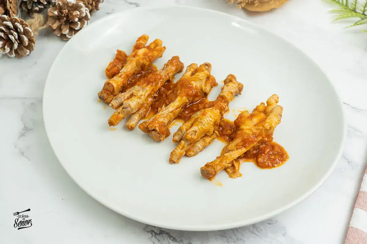 Patas de pollo en salsa roja, servidas en un plato blanco.