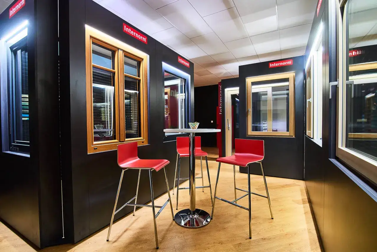 Nowoczesny salon z oknami i drzwiami Internorm, czerwone hokery i stolik.