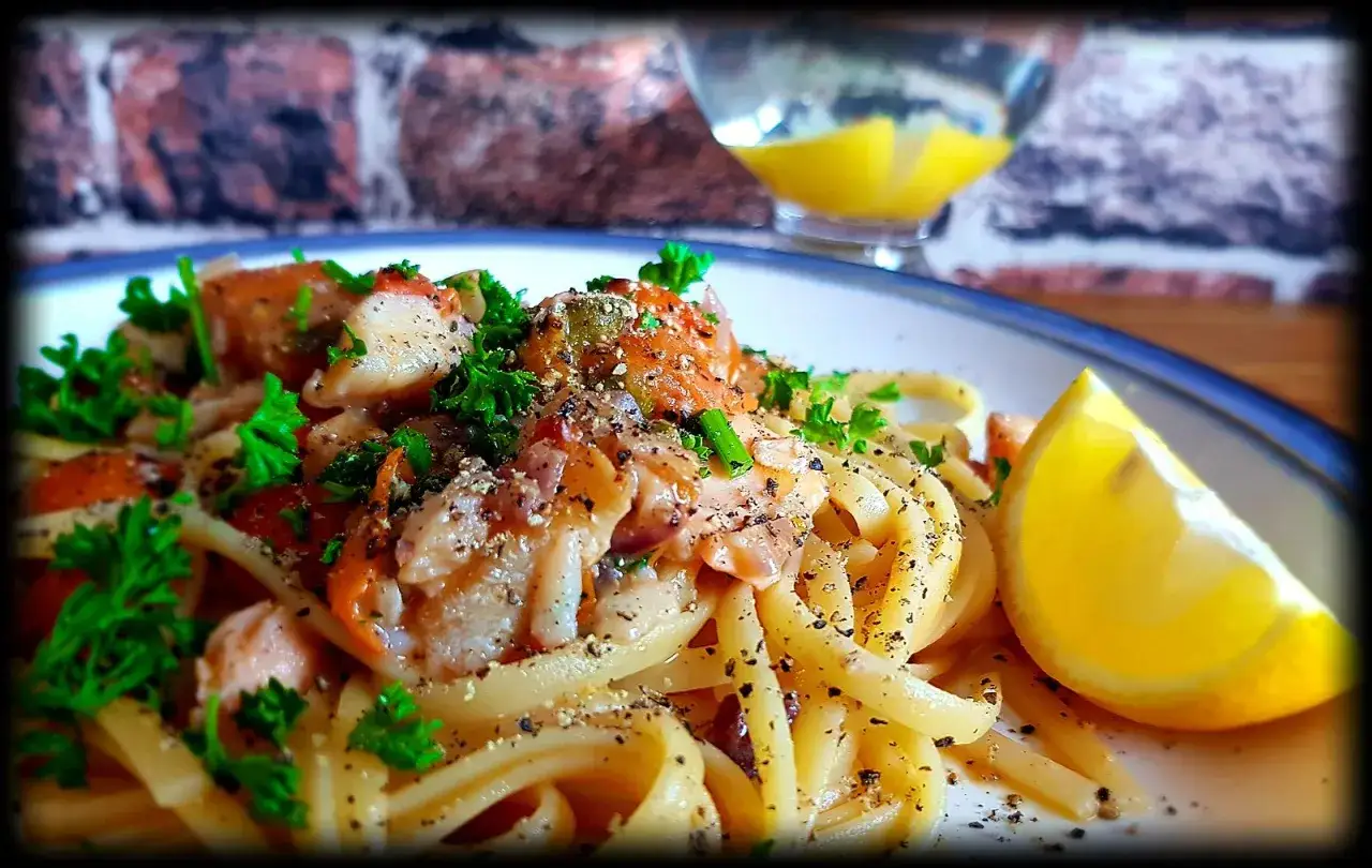 Pyszne Linguine Frutti di Mare przepis na talerzu, udekorowane natką pietruszki i ćwiartką cytryny.