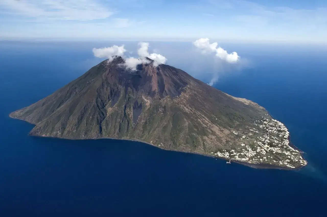 Stromboli, jeden z najbardziej aktywnych wulkanów w Europie, wyrzuca dym nad spokojnym morzem. U podnóża wulkanu rozciąga się malownicza wioska.