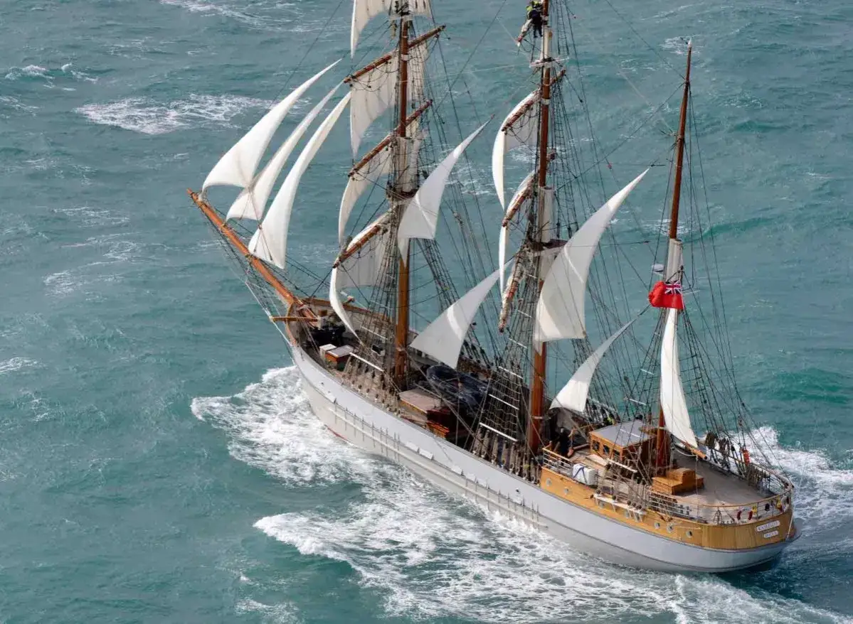 Vue aérienne d'un navire historique aux voiles blanches gonflées par le vent, naviguant sur une mer agitée. Ces grands voiliers évoquent des époques révolues.