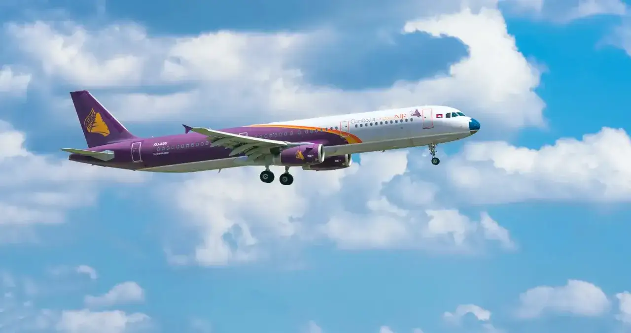 Samolot Cambodia Angkor Air z fioletowym ogonem z symbolem świątyni leci na tle błękitnego nieba z chmurami. Idealny na loty do Kambodży.