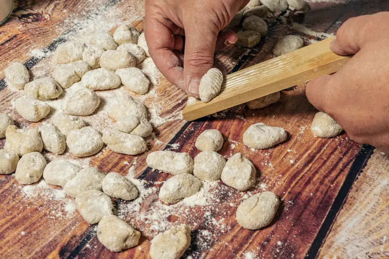 Mani che creano gnocchi su un tagliere di legno. L'impasto gnocchi troppo appiccicoso rende difficile la lavorazione, ma le righe sul legno aiutano a dare forma.
