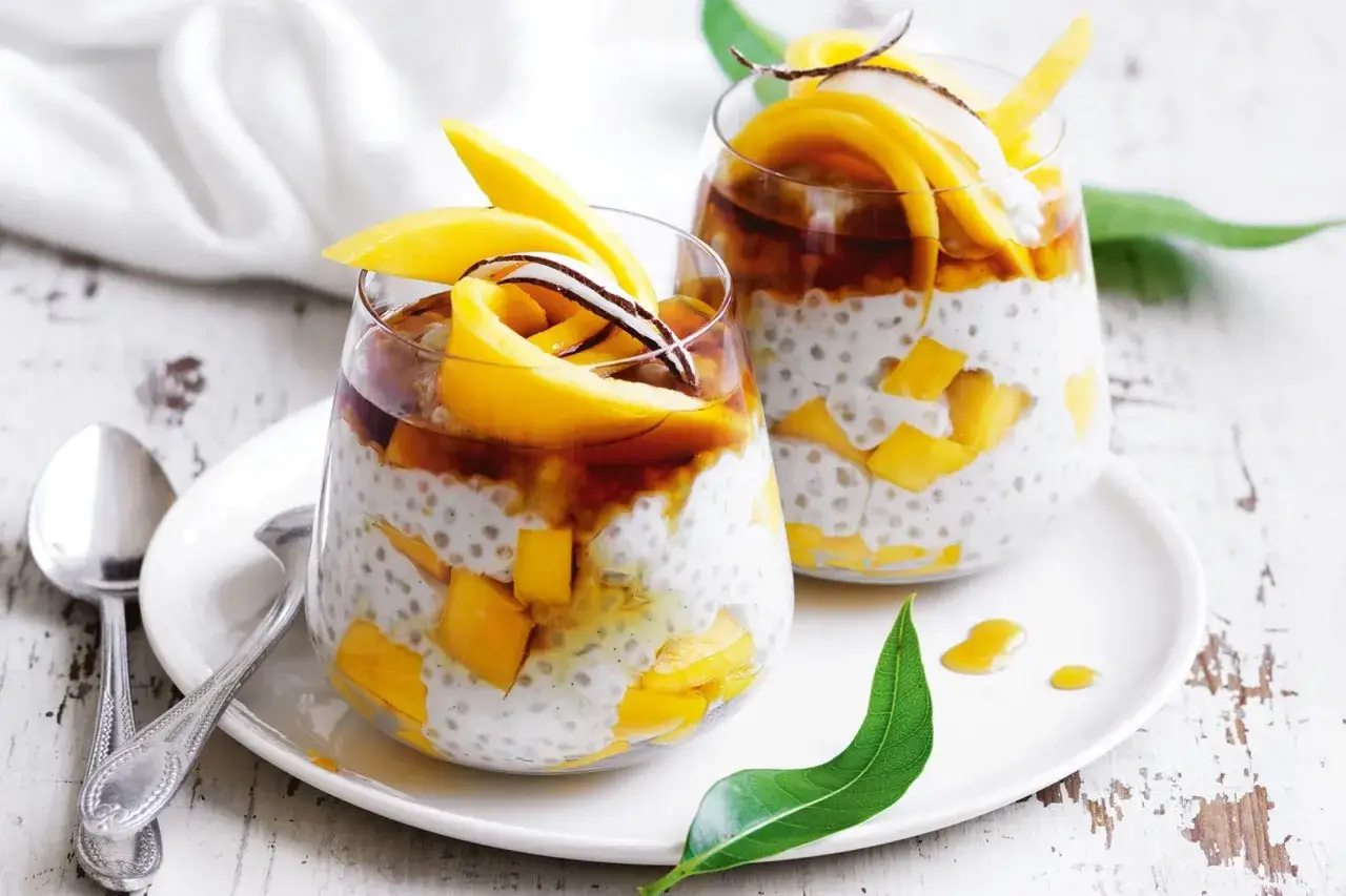 Dwa pucharki z deserem z mleka kokosowego, kawałkami mango i syropem. Idealny tropikalny deser.