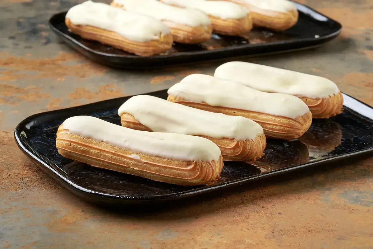 Deliziosi eclair dolci con glassa bianca su piatti neri, pronti per essere gustati.