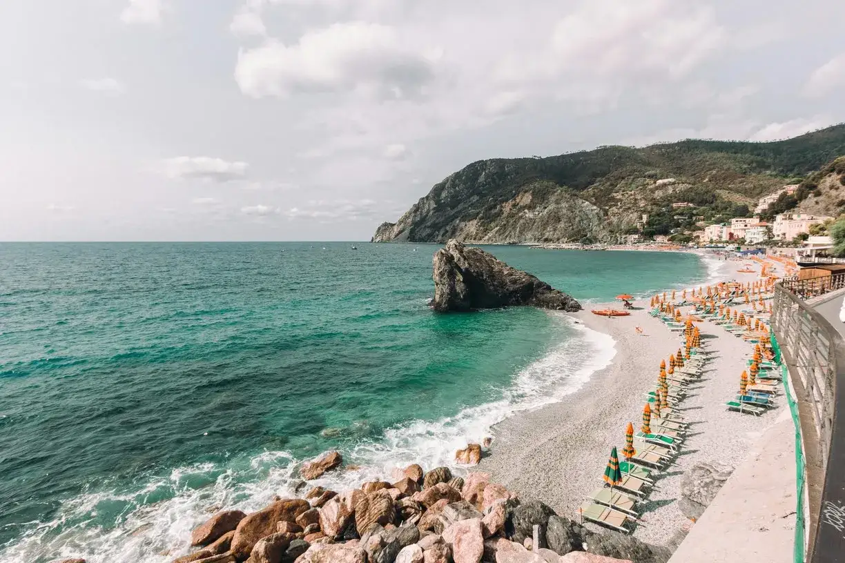 Spiaggia di ciottoli con lettini e ombrelloni colorati, mare turchese e scogliere. Un angolo di paradiso tra le genova spiagge pi&ugrave; belle.