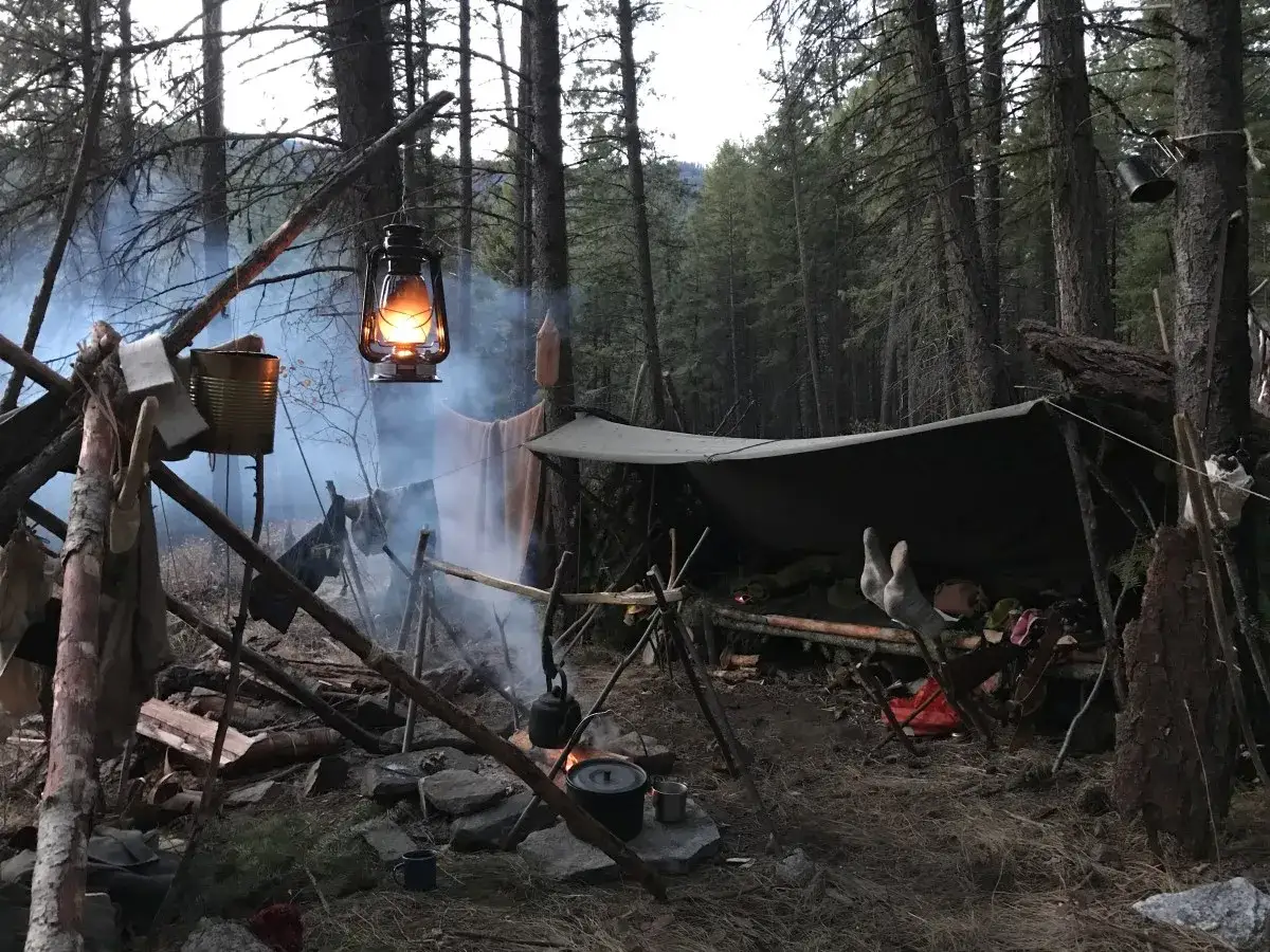 Ognisko i prowizoryczne schronienie w lesie, lampa naftowa oświetla dym. To prawdziwy **bushcraft** – sztuka przetrwania w dziczy.