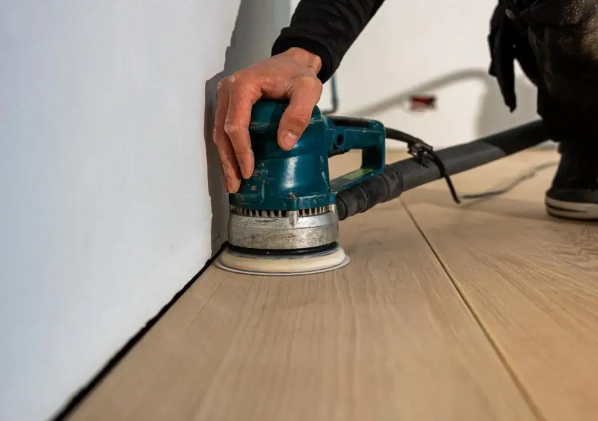 Mano che usa una levigatrice per levigare il parquet, creando una superficie liscia e pronta per la finitura.