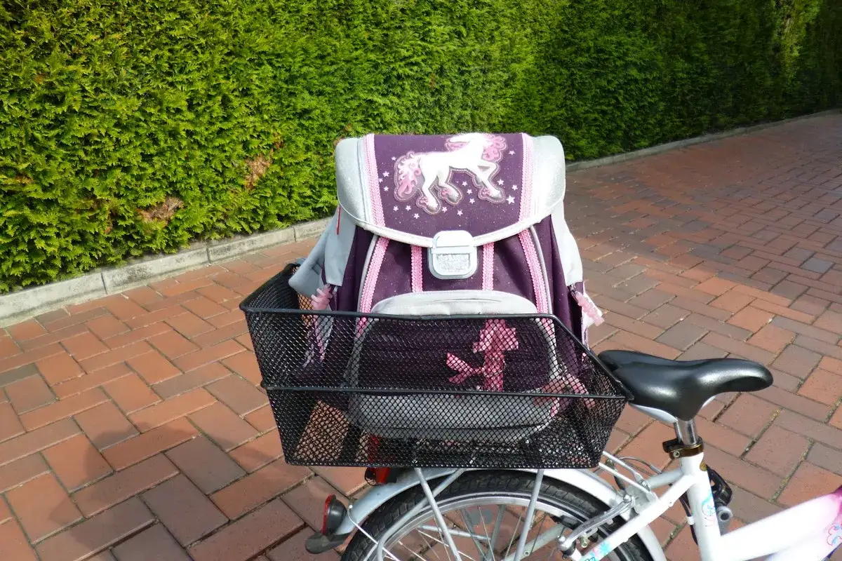 Ein lila Schulranzen mit Einhorn-Motiv ist sicher im Fahrradkorb verstaut. Perfekt, um den Schulranzen auf dem Fahrrad zu transportieren.