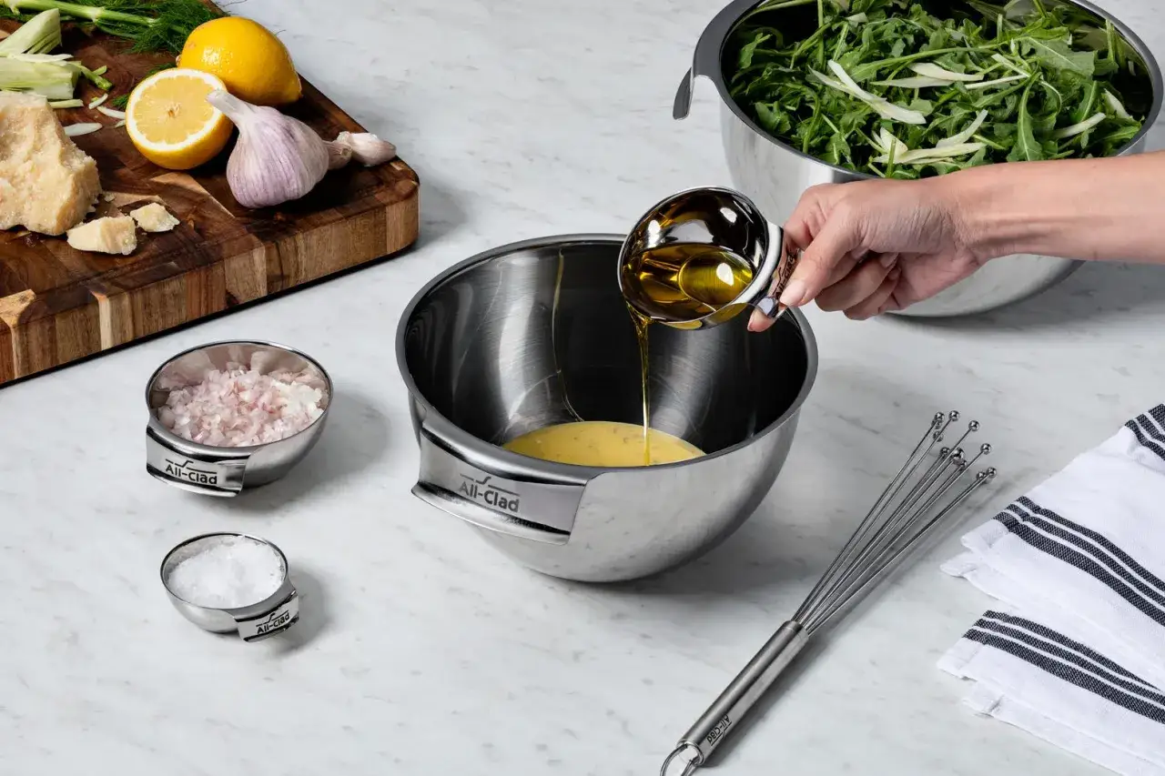 Zutaten f&uuml;r einfache Salat Rezepte werden vorbereitet: &Ouml;l wird in eine Sch&uuml;ssel gegossen, daneben liegen Schalotten, Salz, Zitrone, Knoblauch und Parmesan.