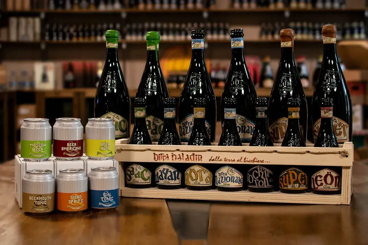 Bottiglie e lattine di birra Baladin, tra cui una birra 14 gradi, in un'ambientazione da negozio.
