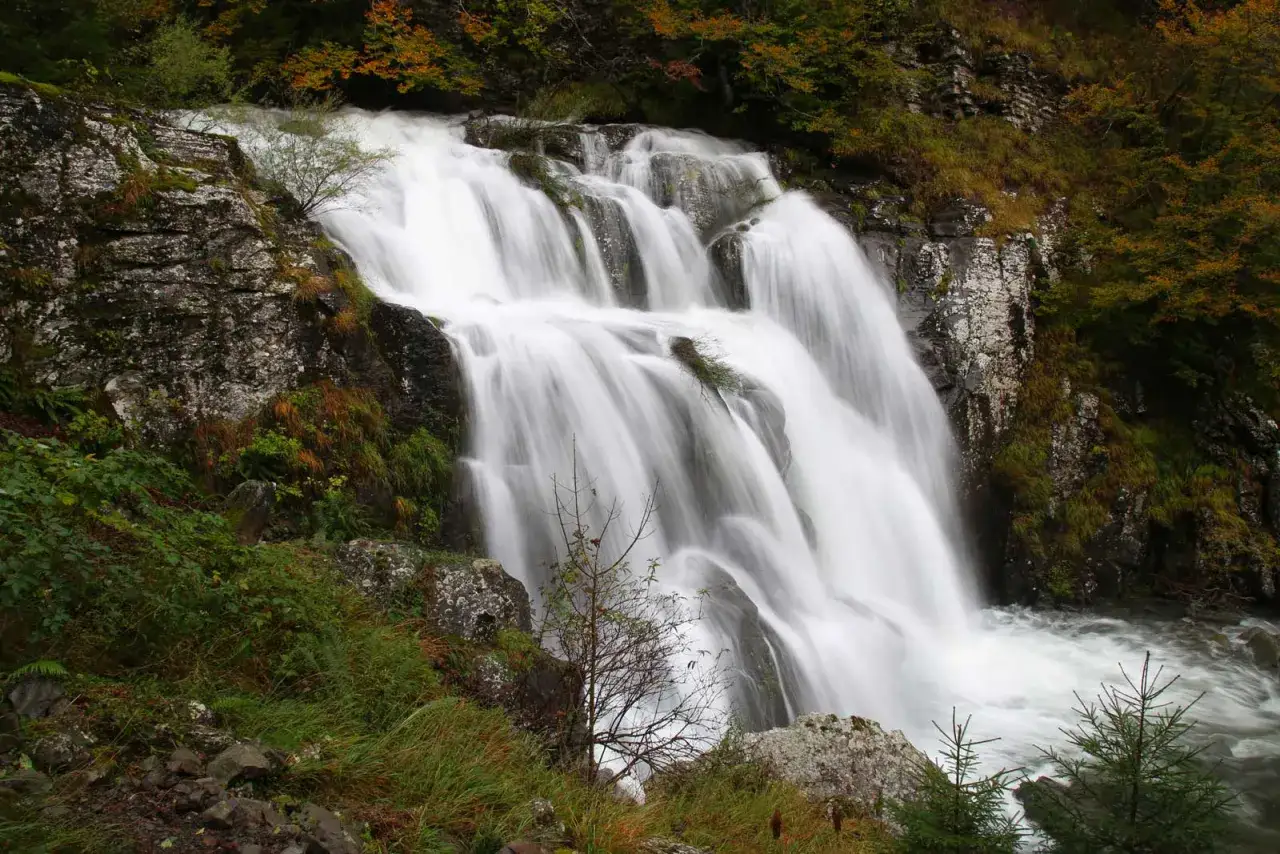 Cascata fragorosa lungo il sentiero delle cascate, con rocce muschiose e vegetazione autunnale.