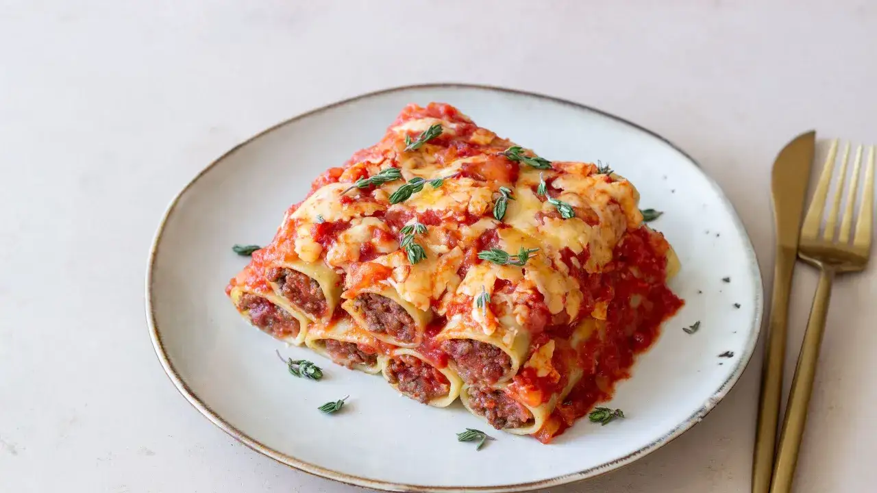 Cannelloni di carne ricetta della nonna, un piatto fumante con sugo rosso e formaggio fuso, guarnito con timo fresco.