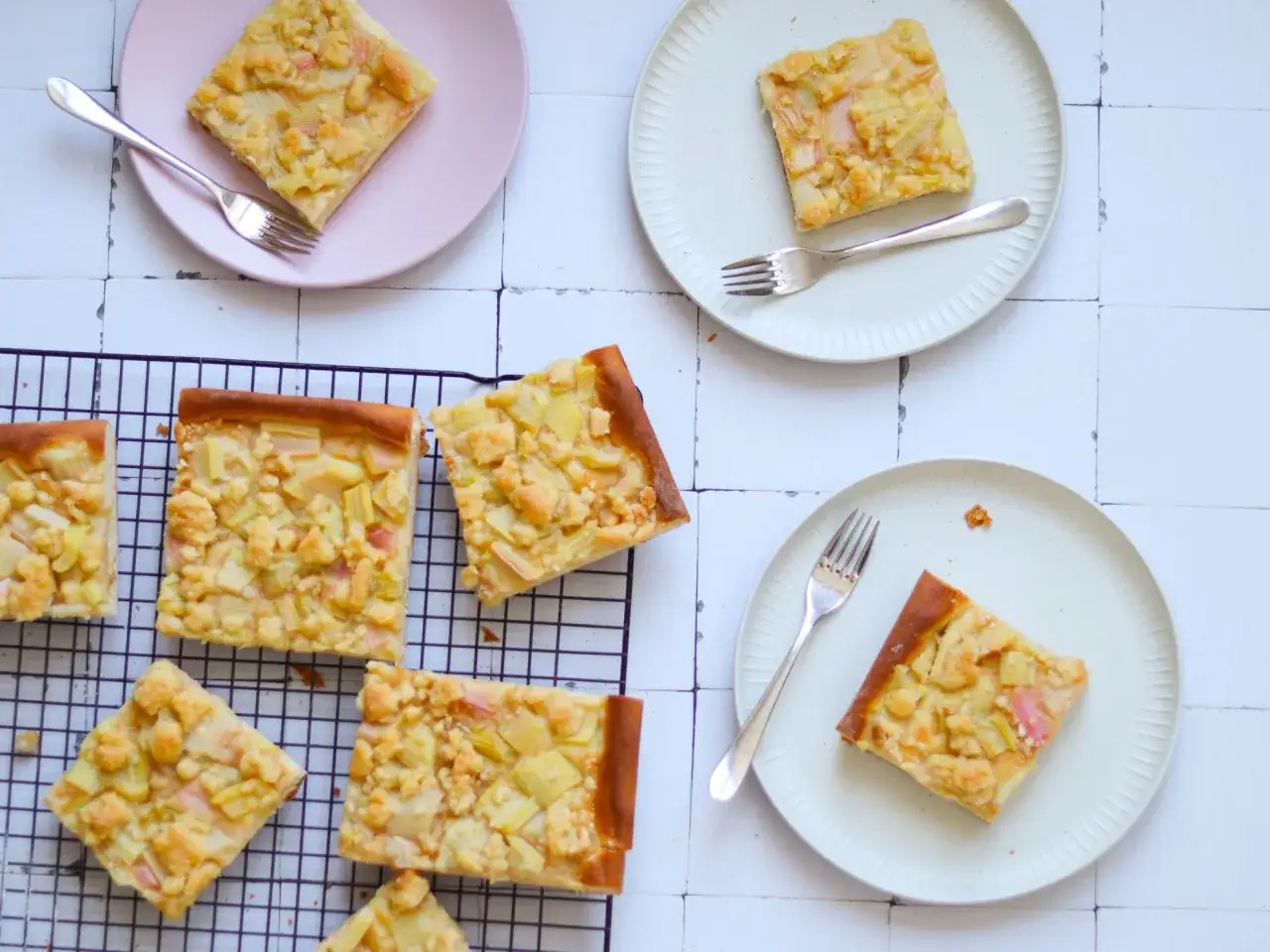 Saftiger Rhabarberkuchen auf Hefeteig, bestreut mit Streuseln, auf Tellern und einem Kuchengitter.