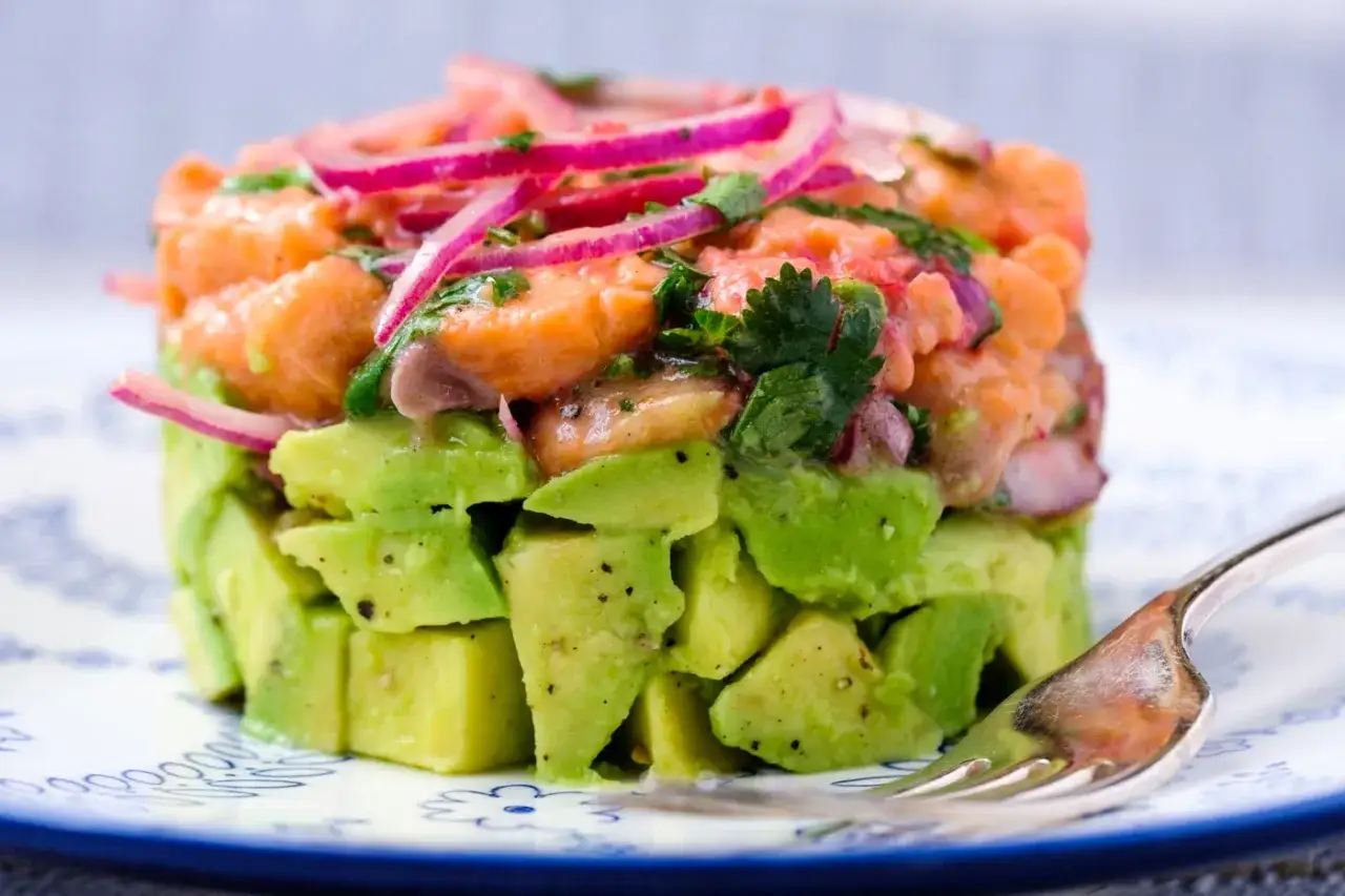 Delicioso tartar de salmón y aguacate, con cebolla morada y cilantro fresco, servido en un plato blanco con borde azul.