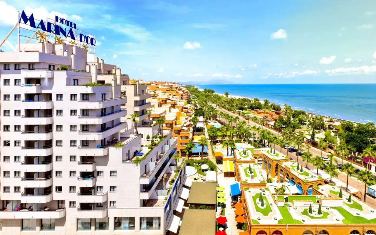 Edificios blancos y naranjas junto al mar en Marina d'Or Ciudad de Vacaciones, con palmeras y piscinas.