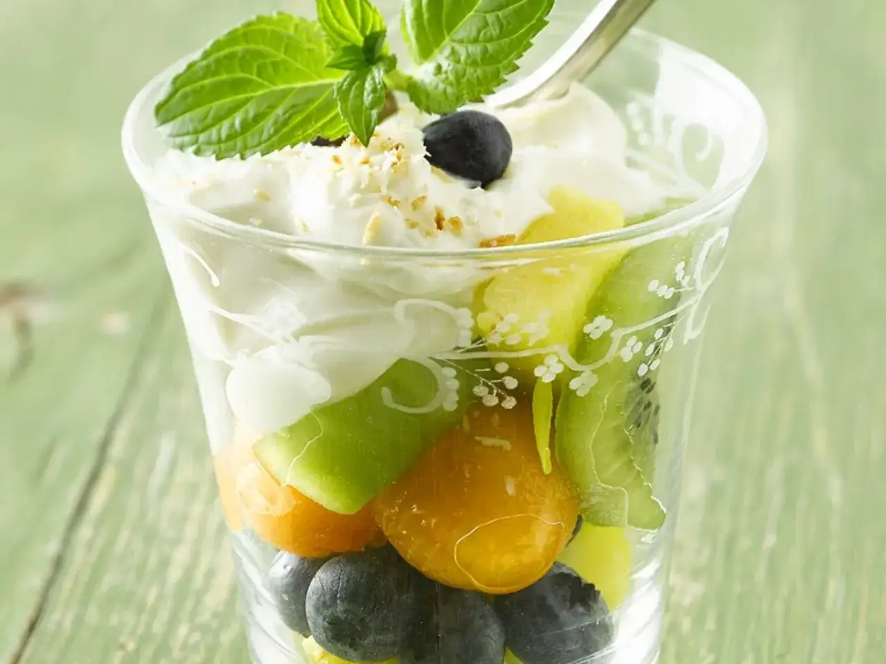 Erfrischendes Kaltschalen-Rezept im Glas: Schichten aus Joghurt, Kiwi, Melone, Ananas und Blaubeeren, garniert mit Minze.