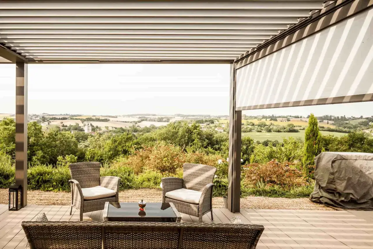 Terrasse am&eacute;nag&eacute;e sous une pergola bioclimatique, avec vue panoramique sur la campagne. Mobilier de jardin confortable.