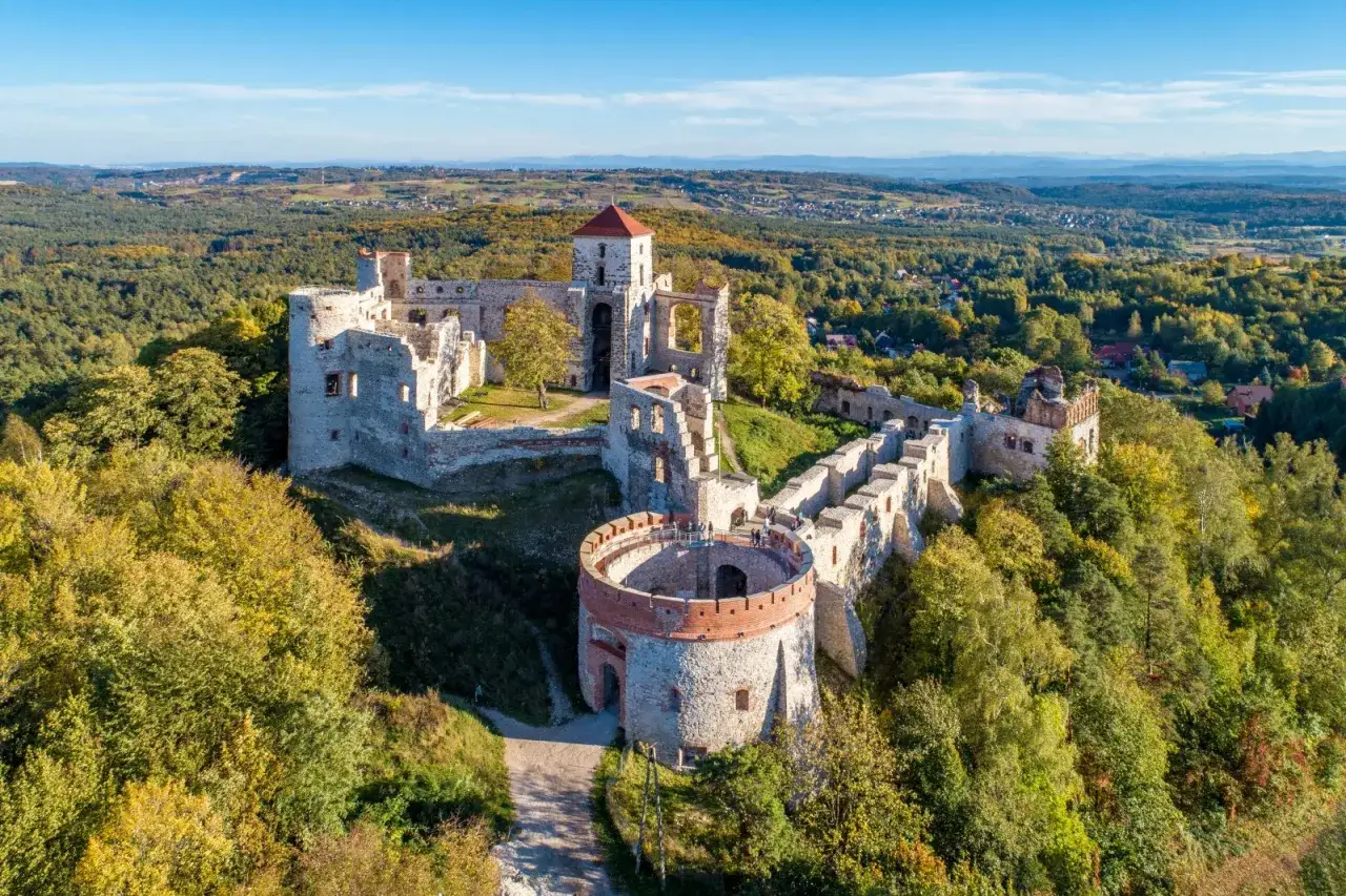 Zamek Tenczyn, malownicze ruiny na wzgórzu, otoczone jesiennym lasem, z widokiem na dolinę i miasteczko.