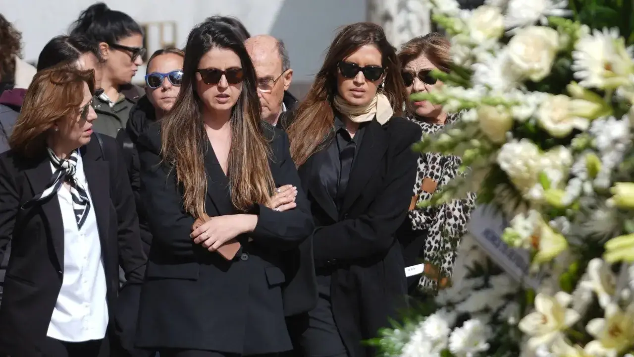 Sara Carbonero, con semblante serio, asiste a un funeral. La acompaña un grupo de personas, todas vestidas de luto.