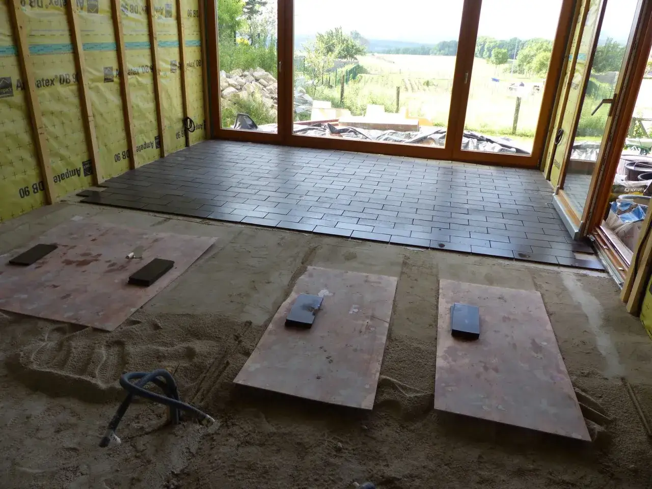 Pose de tomettes sur dalle b&eacute;ton. Le sol est en cours d'installation, avec des tomettes sombres pos&eacute;es sur une dalle de b&eacute;ton, et des plaques de protection sur le sable.