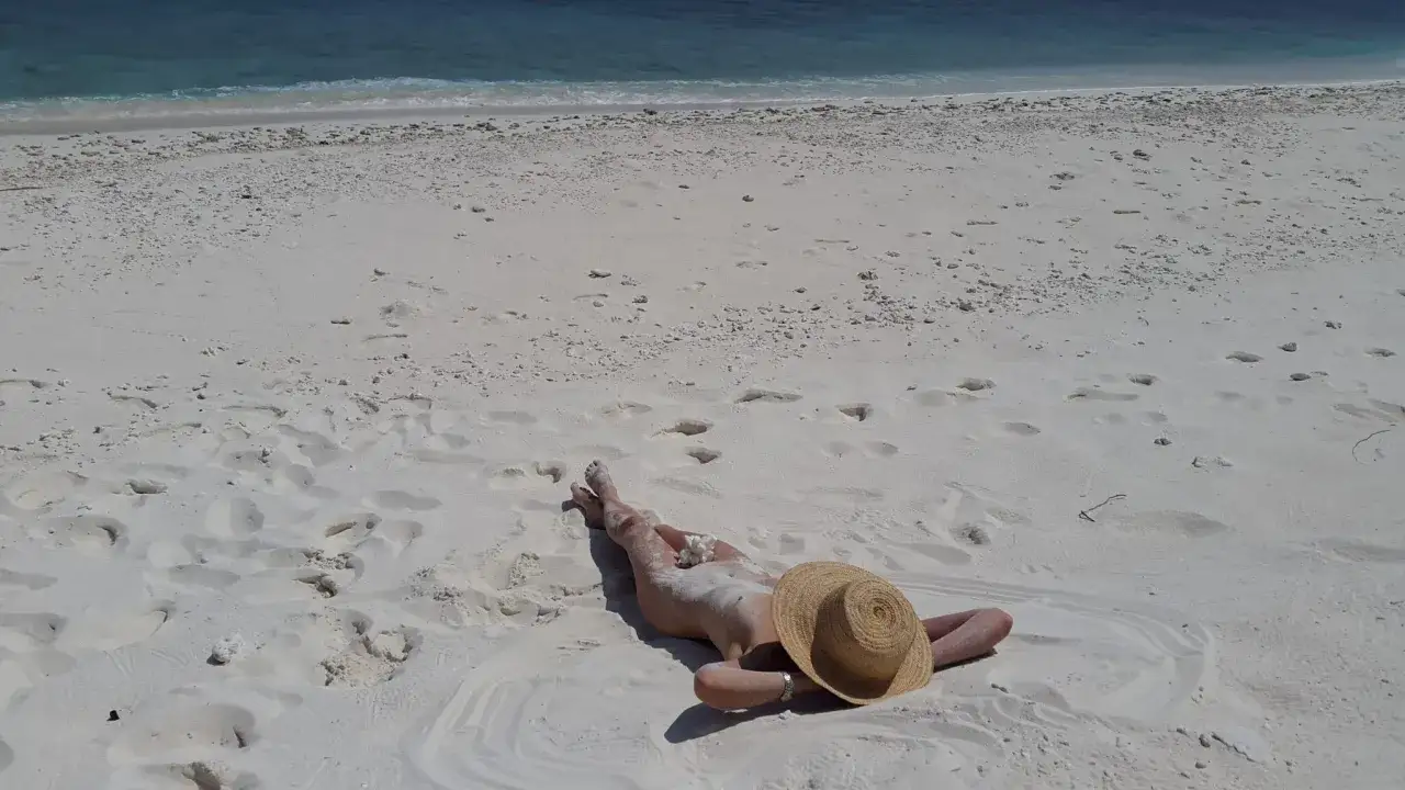 Persona rilassata su una spiaggia di sabbia bianca, con il mare azzurro sullo sfondo. Un'immagine che evoca la tranquillit&agrave; delle spiagge naturiste in Italia.