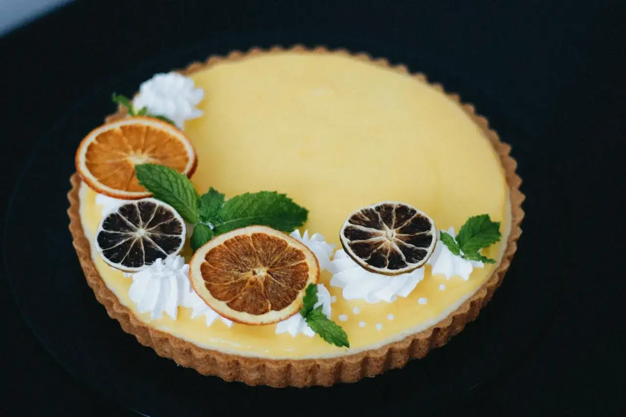 Tarta z kremem cytrynowym, ozdobiona suszonymi plasterkami pomarańczy, limonki, bitą śmietaną i miętą.