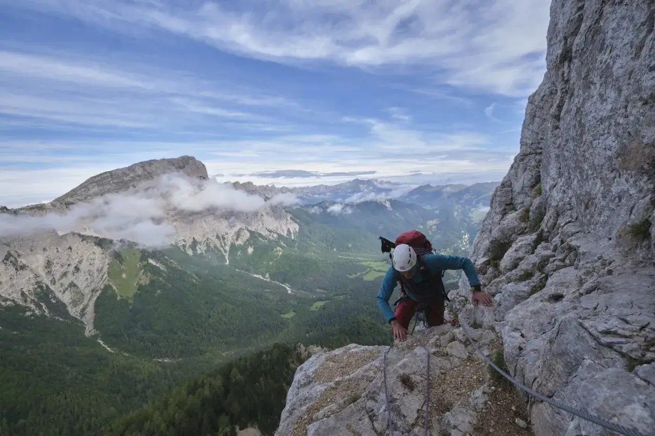 Grimpeur sur un sentier de via ferrata, le pas de l'aiguille. Vue spectaculaire sur les montagnes et la vallée verdoyante.