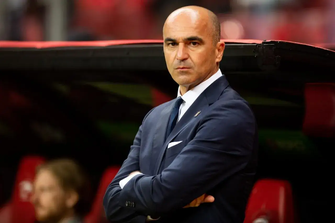 Roberto Martínez, trener Portugalii, w eleganckim garniturze, z rękami skrzyżowanymi na piersi, patrzy z uwagą.