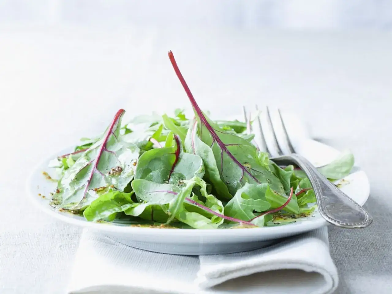 Frischer mangold salat mit roten Stielen, beträufelt mit Dressing, auf einem Teller mit einer Gabel.