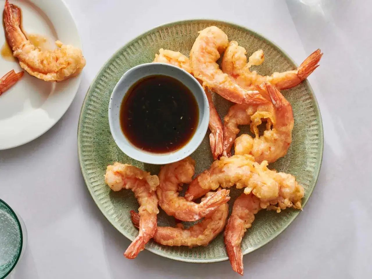 Chrupiące tempura do krewetek na zielonym talerzu, z miseczką sosu. Idealna przekąska.