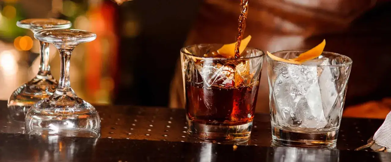 Ein dunkler Whisky wird in ein Glas mit Eis und Orangenzeste gegossen. Die ideale trinktemperatur whisky ist erreicht.