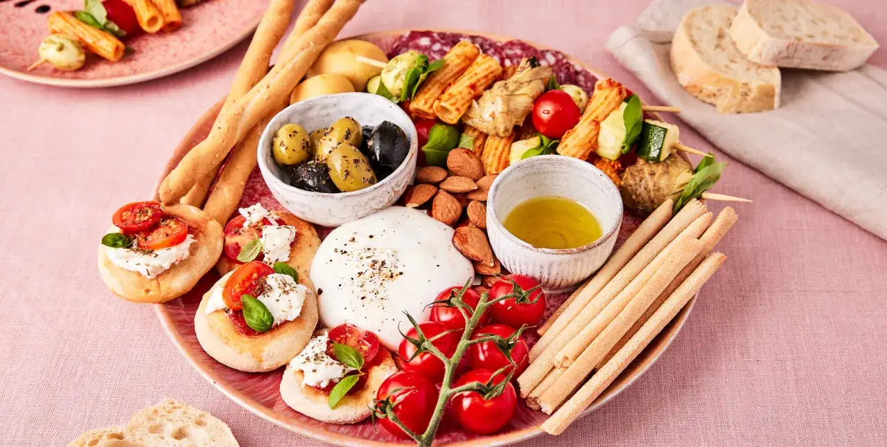 Eine Platte mit italienischen Pasta-Vorspeisen: Bruschetta, Burrata, Oliven, Grissini, Salami und Spieße mit Gemüse und Pasta.