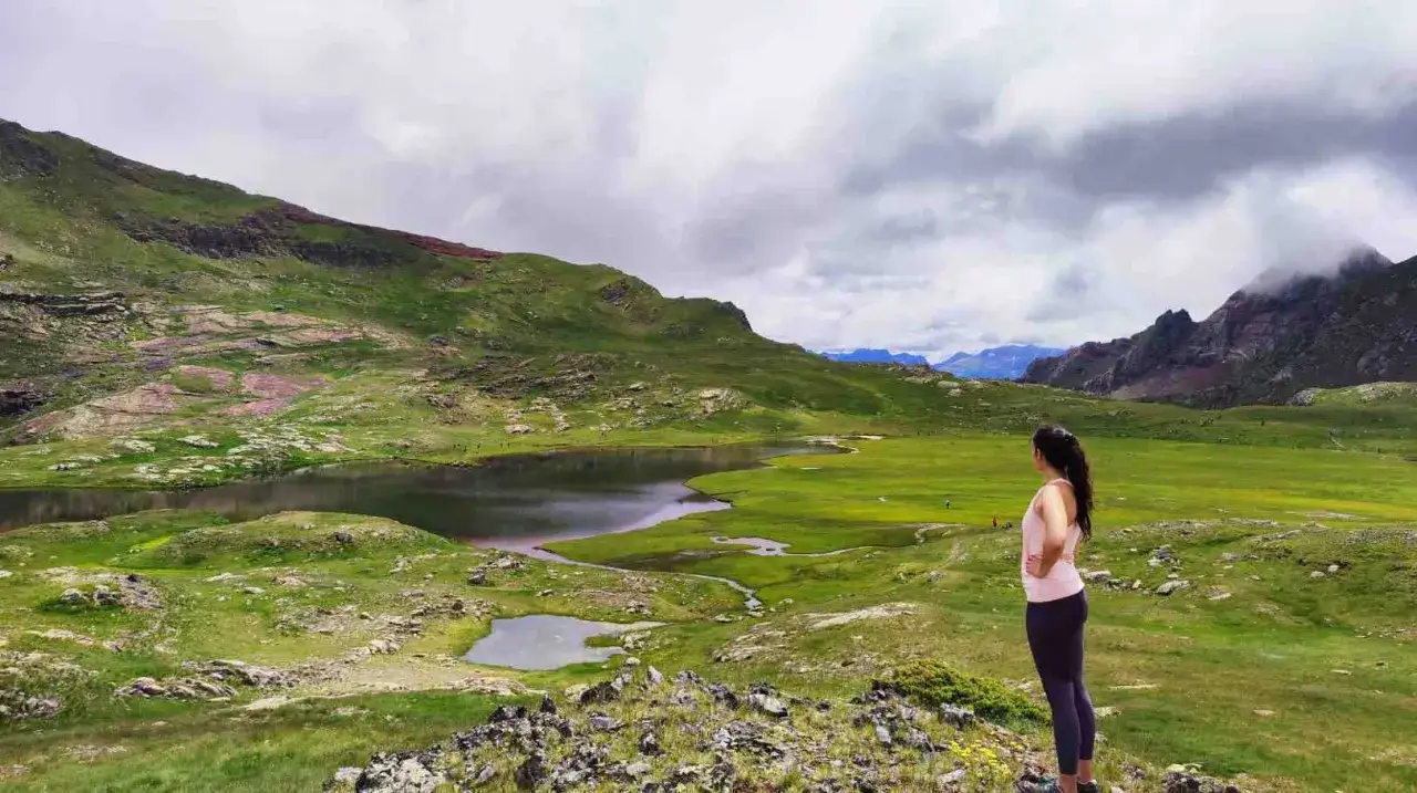 Mujer contempla un lago y prados verdes en el Valle de Tena, ideal para rutas de senderismo.