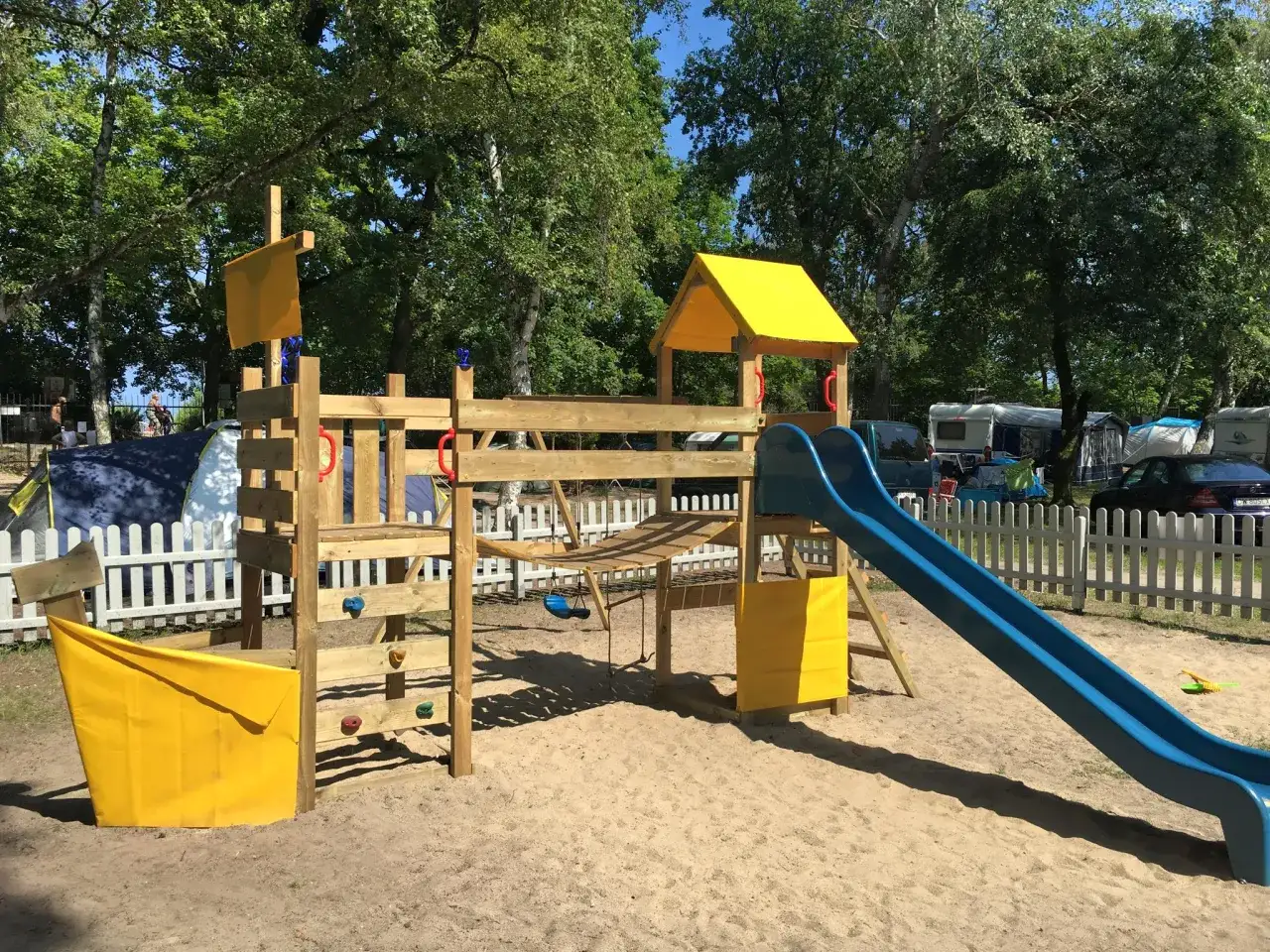 Drewniany plac zabaw z żółtymi elementami i zjeżdżalnią. Idealne miejsce dla dzieci przy restauracji w Gdańsku.