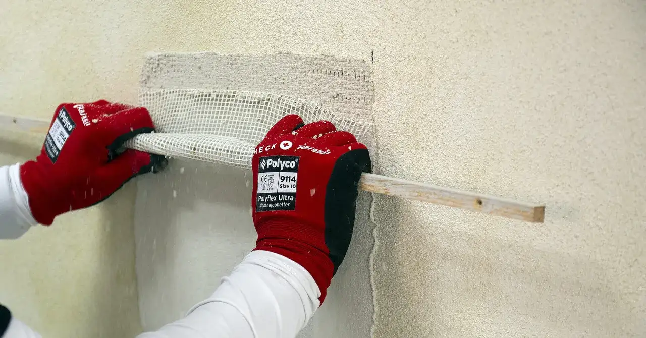 Rote Handschuhe mit wei&szlig;em Netzgewebe und Holzleiste an einer Wand. F&uuml;r das Fassade streichen ist Grundierung notwendig, um eine gute Haftung zu erzielen.