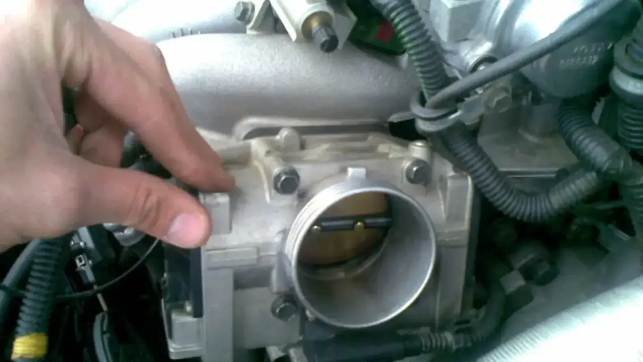 Mano ajustando la **válvula mariposa coche**, parte del sistema de admisión de aire del motor.