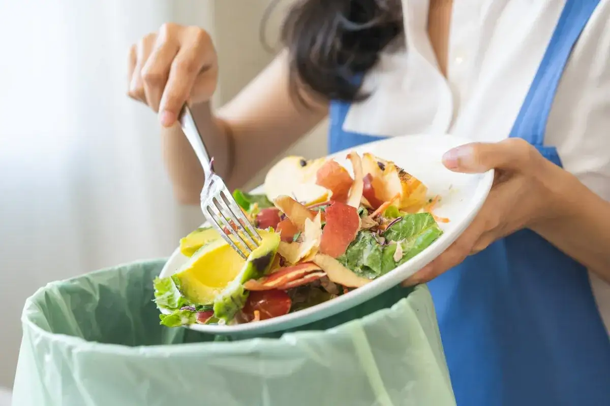 Persona separando restos de comida, como cáscaras de manzana y aguacate, para el reciclaje orgánico.