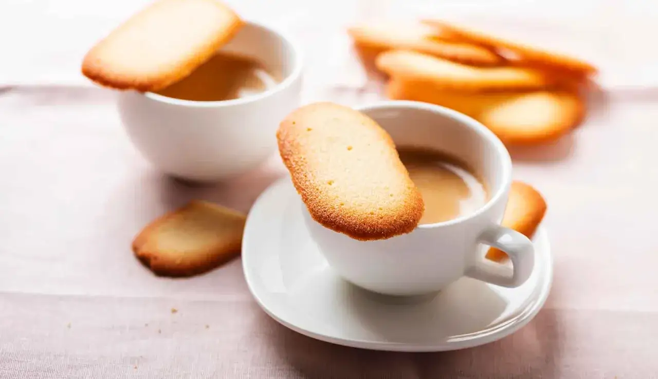 Deliziose lingue di gatto dorate appoggiate su tazze di caffè fumante, un invito alla dolcezza.