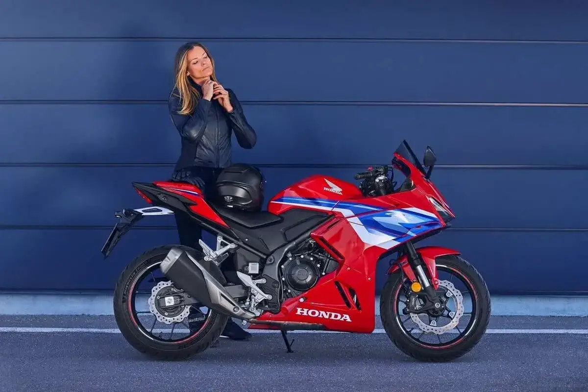 Mujer con chaqueta de cuero junto a una moto Honda roja. Ideal para saber que motos puedo conducir con el a2.