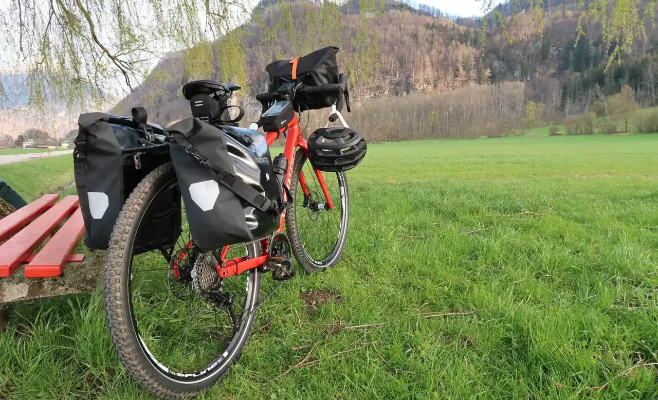 Rotes Fahrrad mit Packtaschen für Bike Packing steht auf einer grünen Wiese. Helm hängt am Lenker.