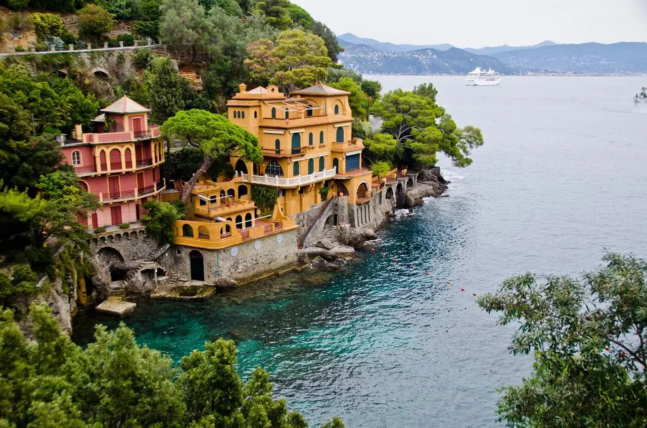 Villas color&eacute;es sur la c&ocirc;te rocheuse de Santa Margherita Ligure, Italie, avec une mer turquoise et un paquebot &agrave; l'horizon.
