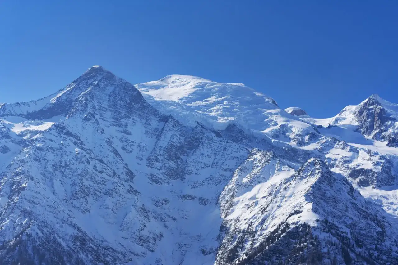 Majestatyczne, ośnieżone szczyty Alp, w tym Mont Blanc, dominują na tle błękitnego nieba. To jedne z najwyższych szczytów Europy.