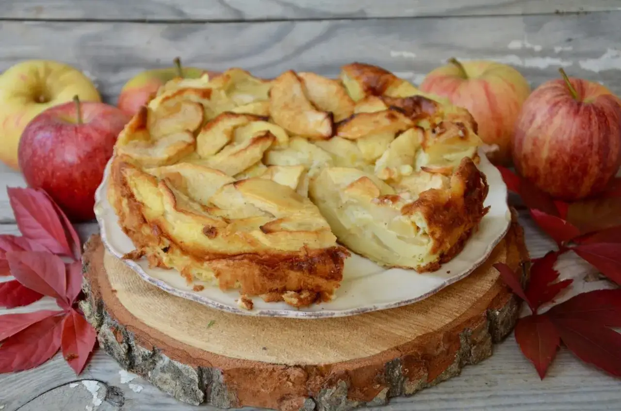 Un délicieux clafoutis aux pommes, doré et moelleux, entouré de pommes fraîches et de feuilles d'automne.