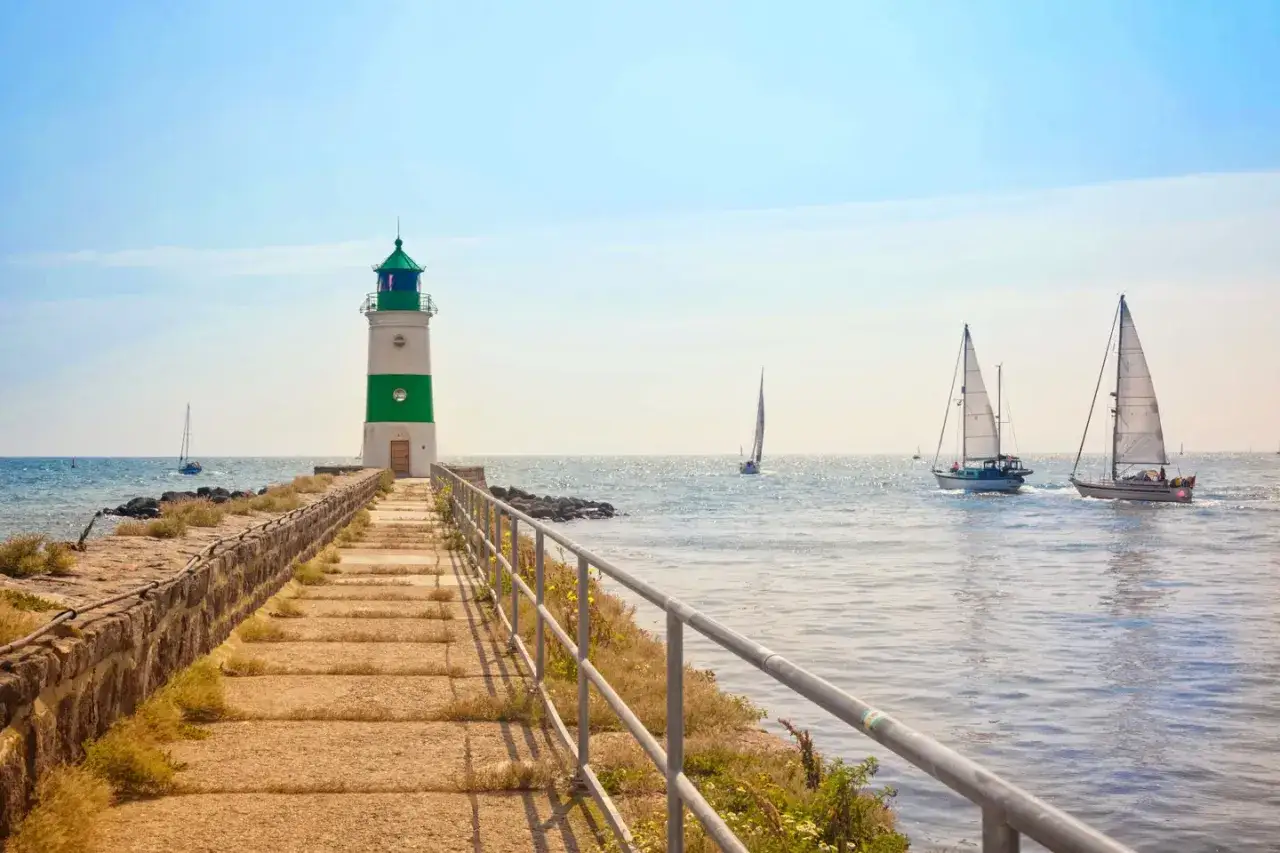 Leuchtturm mit gr&uuml;nen Streifen und Segelboote auf dem Meer. Ein perfekter Ort f&uuml;r fotospots schleswig holstein.
