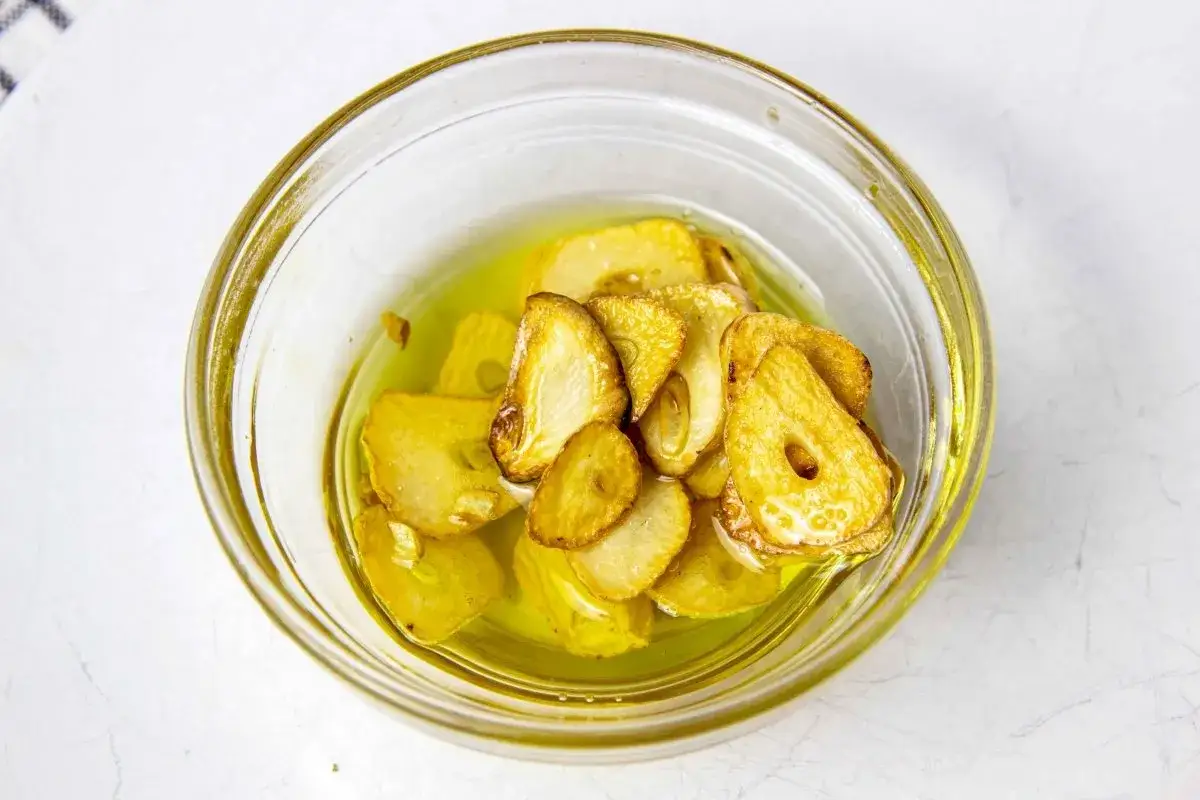 Ajo laminado dorado en aceite de oliva, listo para añadir sabor a tu rape a la plancha.