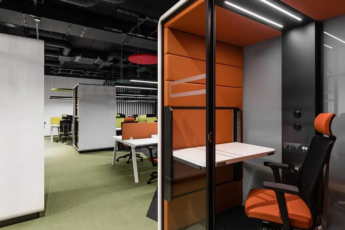 Cabine individuelle orange et grise pour l'isolation acoustique de bureau. Siège ergonomique, table rabattable et éclairage intégré.
