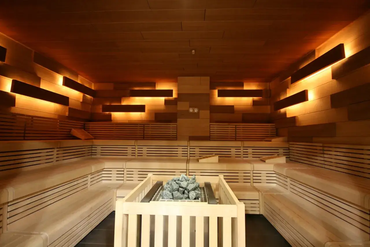 Holzverkleidete Sauna mit mehreren Ebenen, warmem Licht und einem Steinofen &ndash; eine perfekte badezimmer wellness oase.