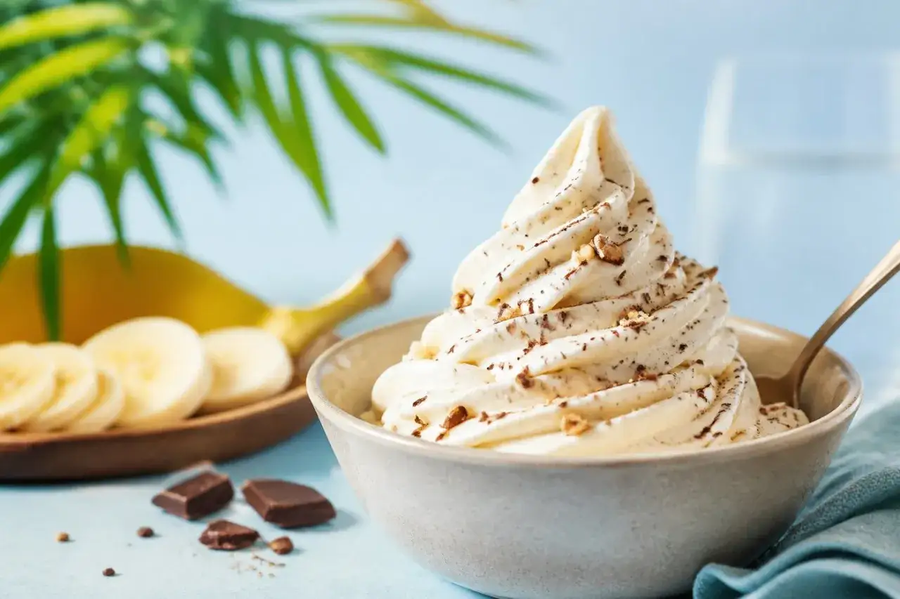Ein cremiges Softeis mit N&uuml;ssen und Schokost&uuml;ckchen, daneben Bananenscheiben und Schokolade &ndash; die perfekten Softeis Zutaten f&uuml;r einen Genussmoment.