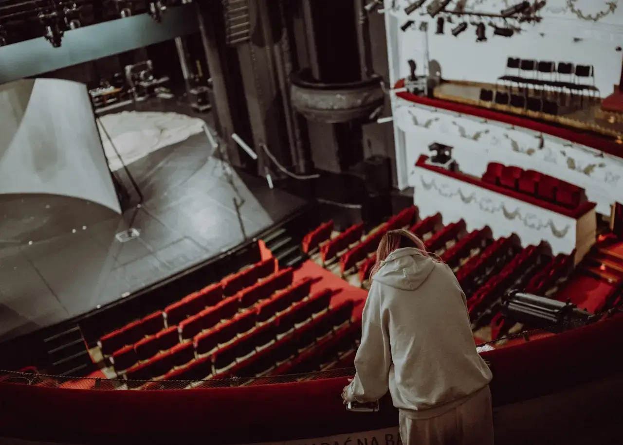 Widok na pustą salę teatralną w Warszawie. Dziewczyna w bluzie z kapturem obserwuje scenę.
